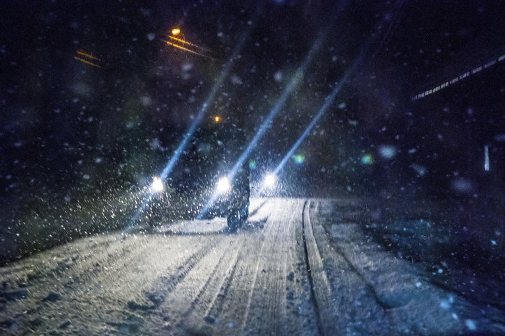 Snowstorm at night with a car, headlights on, driving through it