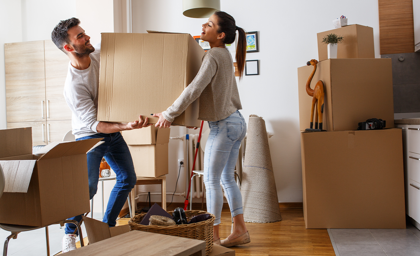 Young couple, surrounded by move-in boxes, carry more boxes into their new home