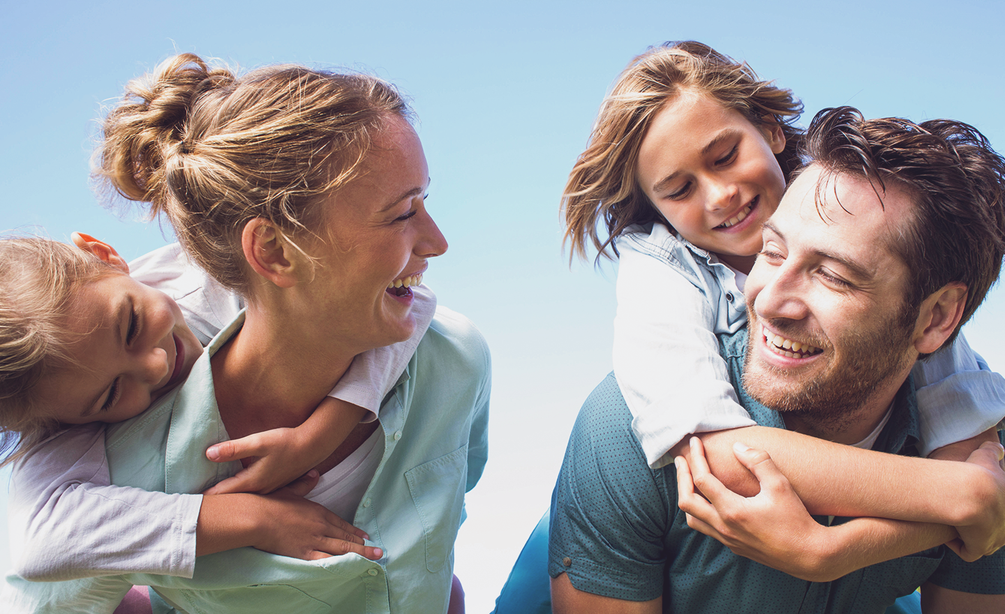 Happy joyous husband and wife give piggy backs to two young daughters