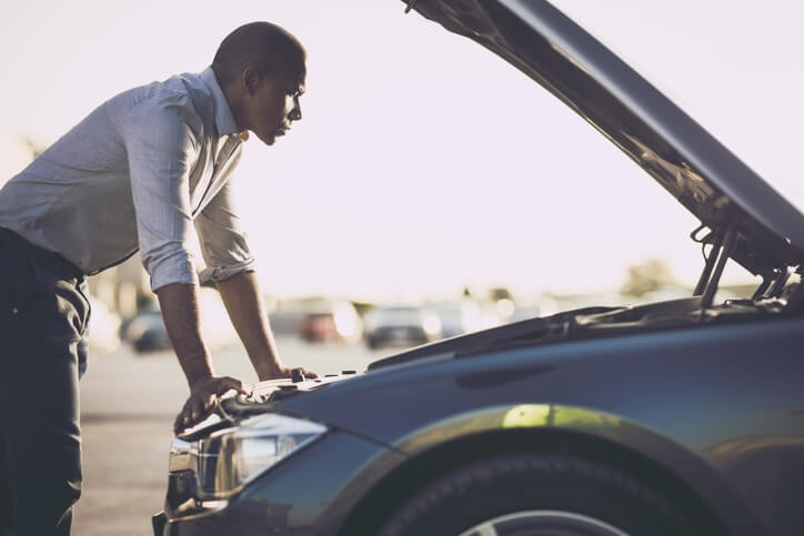 Young man looks under the hood of his car