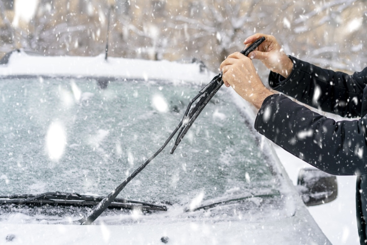 Man cleans windshield wiper blades on his vehicle during snow showers