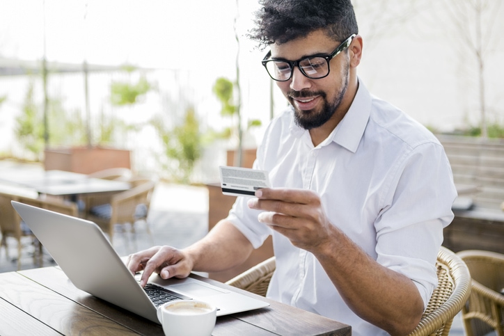 Young man sits at his laptop and looks at his credit card