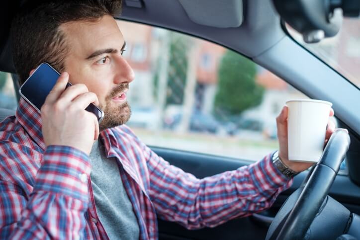 Man distracted while driving with a coffee in one hand and talking on the phone with the other hand