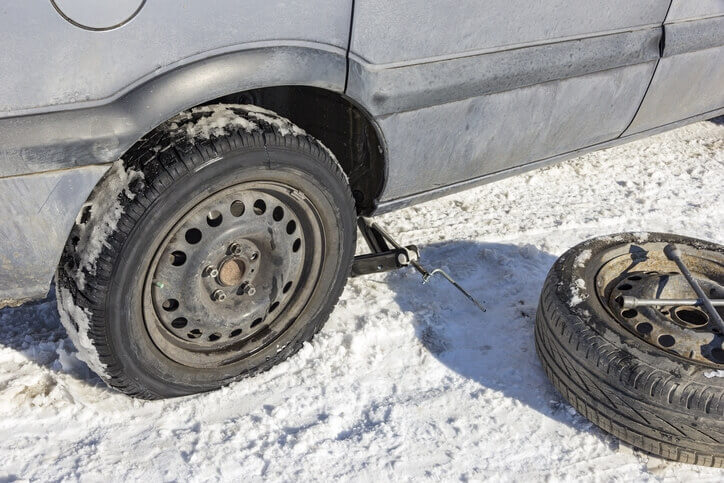 Flat tire on car being replaced on winter road