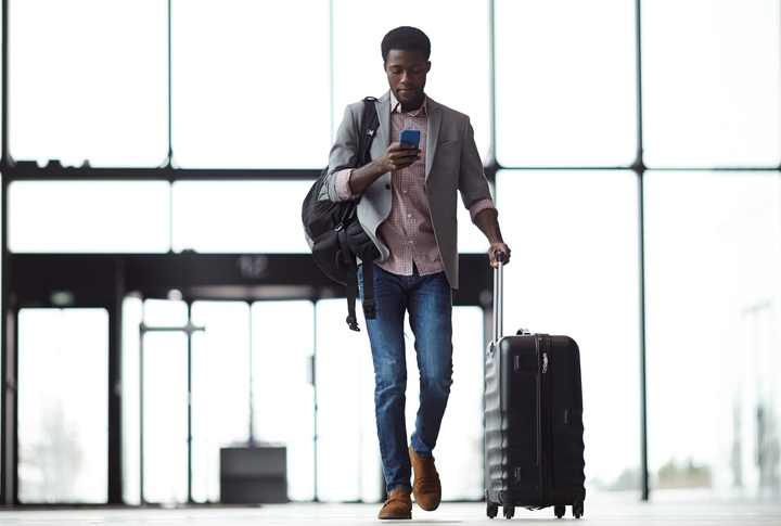 Young man entering an airport, looking at his phone getting ready to travel.