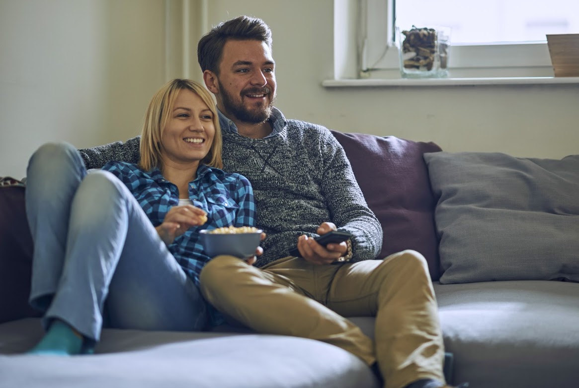 Young couple relax on the couch with a snack and the television remote