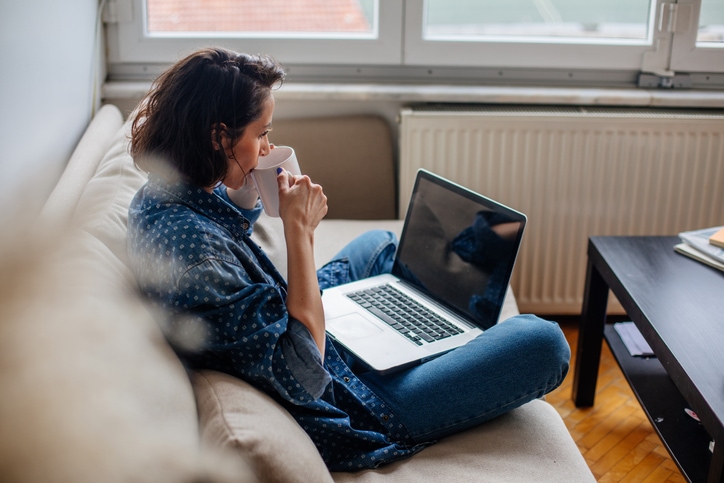 Young woman sips coffee, looking at her laptop