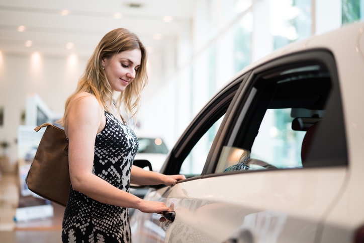 Young woman shopping for a new vehicle, looking into white sedan. 