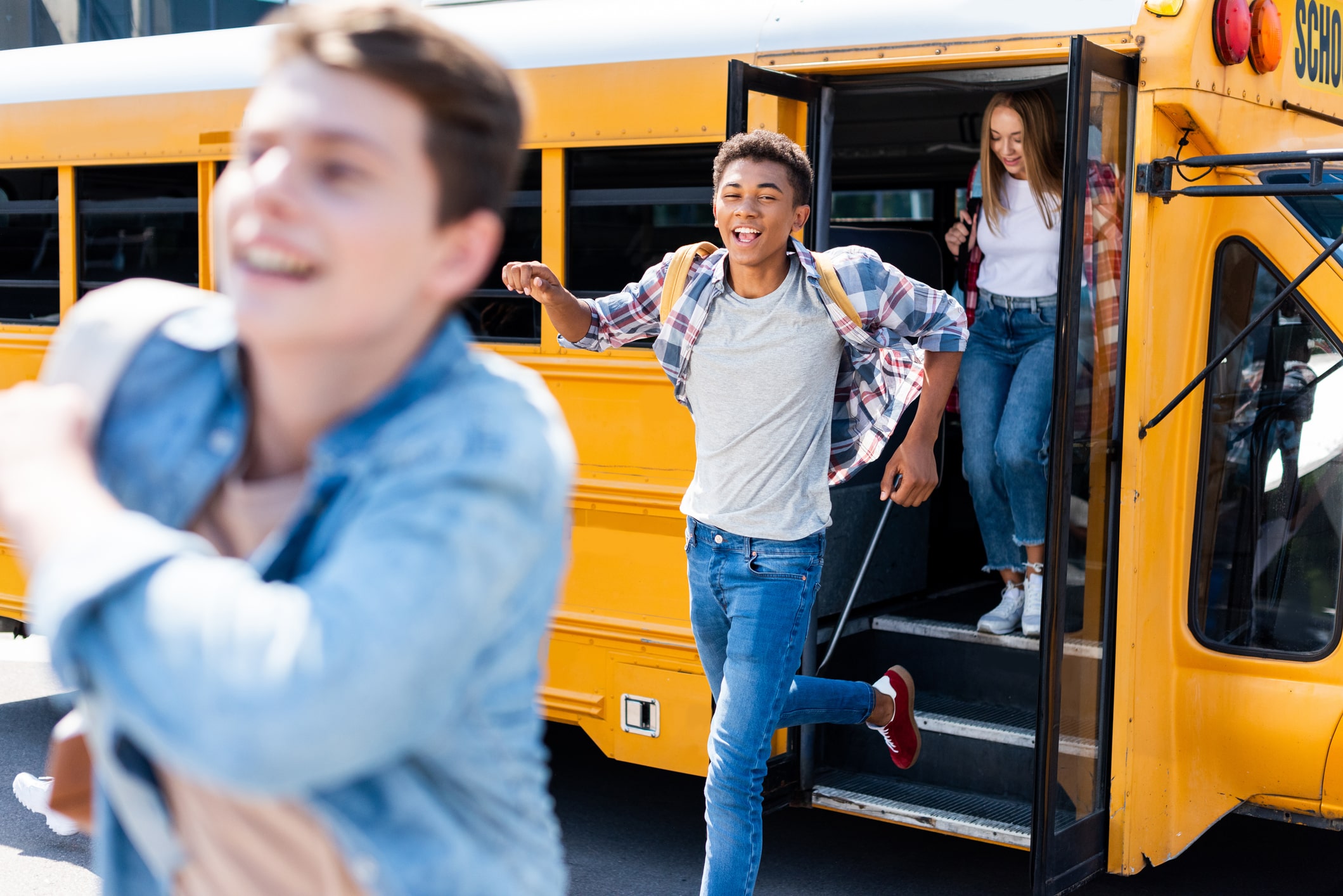 Three young people are seen descending from the steps of a yellow school bus
