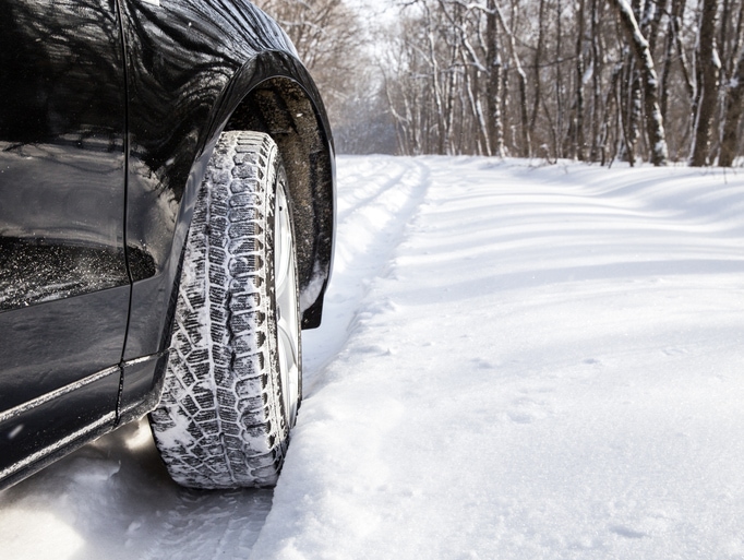 Low angle shot of a vehicle's snowy tire on a wintry forested road