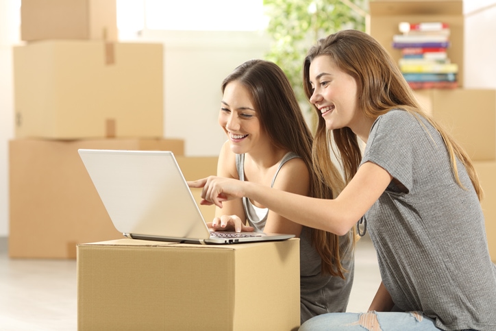 Two young women moving into apartment, looking at their laptop