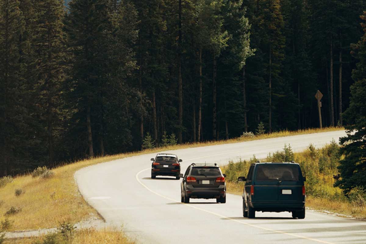 Three vehicles drive down a mountain, forested road